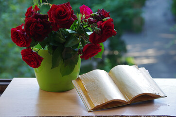Canvas Print - An open book, a bouquet of red roses on the windowsill.