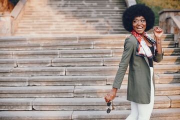 Wall Mural - Fashionable girl in a summer city. Black lady in a green jacket. Woman in a red scarf. Famale with sunglasses