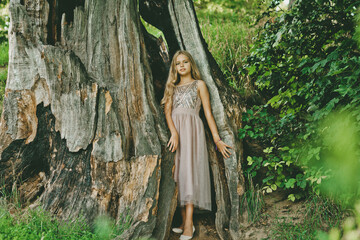 Pretty caucasian girl posing near tree on summer day. Lovable long-haired blonde girl on a nature background.