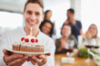 Junger Mann schenkt Kuchen mit Kerze zum Geburtstag