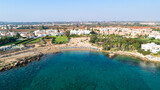 Fototapeta Desenie - Aerial bird's eye view of Sirena beach in Protaras, Paralimni, Famagusta, Cyprus. The famous Sirina bay tourist attraction with sunbeds, golden sand, restaurant, people swimming in the sea from above.