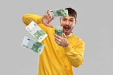 People Concept - Happy Young Man In Yellow Sweatshirt Pouring Money Over Grey Background