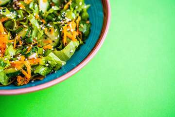 Fresh vegetable salad on a green background. Salad of fresh cucumbers, lettuce, carrots, green onions and sesame seeds. Diet salad
