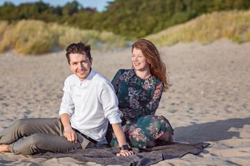 Young couple relax in the sand in clothes on the seashore, laugh and talk