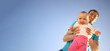 © Sk Elena - Father holds a small child in his arms on a background of a summer blue sky. Cute baby is smiling. Happy family outdoors. Left space for text.