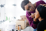 African American woman applying make-up by make-up artist at beauty saloon.