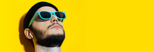 Panoramic Banner View, Portrait Of Young Hipster, Looking Up, Using Wireless Earphones, Wearing Shades Of Aqua Menthe Color On Background Of Yellow With Copy Space.