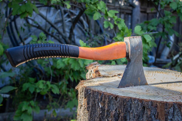 An old ax with an orange handle sticks out in a sawn tree