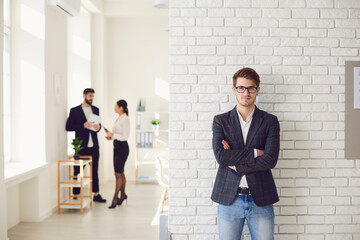 Serious businessman in casual attire standing in a white office on a white wall.