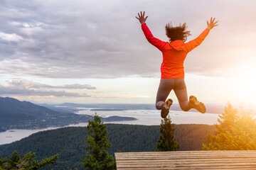 Wall Mural - Adventurous Girl Jumping with Joy on top of a mountain with a beautiful Canadian Nature Background. Taken in Bowen Island, near Vancouver, British Columbia, Canada.