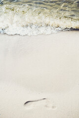 Human footprint in the sand of river with water and waves. Vertical view. Calm summer vacation near water