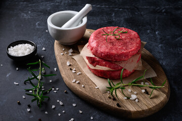 Wall Mural - Raw ground beef meat burger steak cutlets with salt and rosemary on dark background