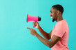© Carlos David - Portrait of a smiling young man with megaphone pointing and looking at copy space