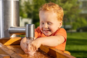 Little boy happily playing with tap water in a sunny playground