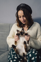 Wall Mural - Lovely woman playing with Siamese cat at home. Friendship between humans and animals