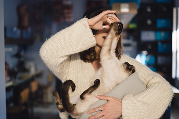 Wall Mural - Lovely woman playing with Siamese cat at home. Friendship between humans and animals