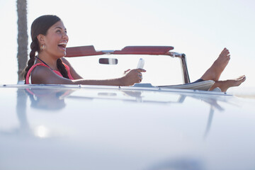 Wall Mural - Laughing girl using cell phone in convertible