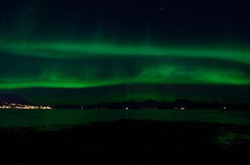 beautiful aurora borealis over fjord and land in tromsoe