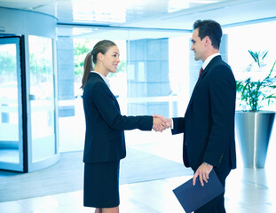 Wall Mural - Smiling businessman and businesswoman handshaking in lobby