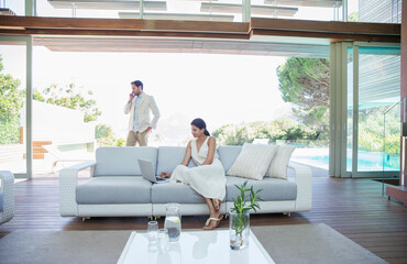 Couple using cell phone and laptop in living room