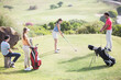 Friends watching woman teeing off on golf course