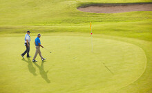 Senior Men Walking Toward Flag And Hole On Golf Course