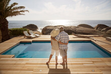 Senior Couple Hugging By Modern Pool Overlooking Ocean