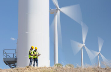 Workers talking by wind turbines in rural landscape