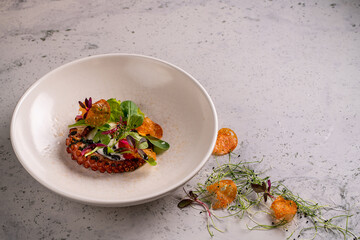 Canvas Print - Close-up of grilled octopus dish plate served with greens and tomato salad on white plate in soft-focus in the background