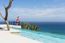 Woman Standing On Poolside Balcony Overlooking Ocean