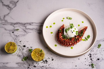 Poster - Close-up of grilled octopus dish plate served with greens and tomato salad on white plate in soft-focus in the background