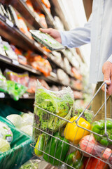 Canvas Print - Close up of man holding full shopping basket in grocery store