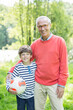© Tom Merton/KOTO - Grandfather and grandson smiling outdoors with soccer ball