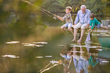 Grandfather Grandsons Fishing Playing With Toy Sailboat At Lake