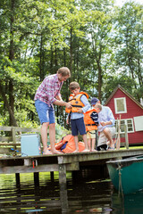 Wall Mural - Father and grandfather fastening life jackets on boys