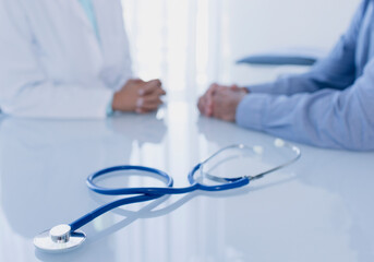 Wall Mural - Stethoscope on white desk in doctor's office, female doctor patient sitting 