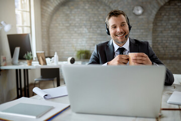 Wall Mural - Happy businessman drinking coffee while having video call in the office.