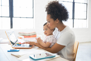 Mother working from home with daughter sitting on her lap