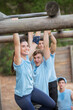 © Sam Edwards/KOTO - Smiling woman crossing monkey bars on boot camp obstacle course