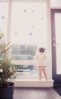 © Monashee Alonso/KOTO - Curious girl on window ledge below Christmas ornaments