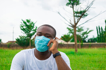 Wall Mural - young black man wearing a nose mask, sitting down and using his smartphone