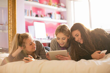 Teenage Girls Using Cell Phones And Digital Tablet On Bed