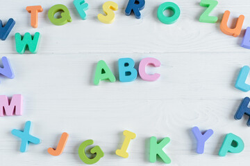 Wall Mural - Close up Multicolored wooden letters with ABC on white wooden background. Set of toys for studying alphabet. Education, back to school concept. Top view, copy space
