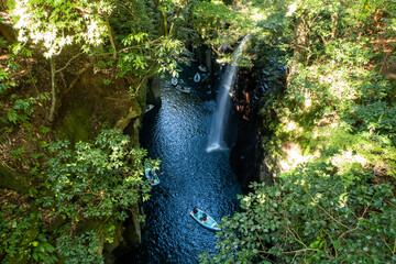 View from a cliff above of Takachiho Gorge with waterfall, boats and green trees on Kyushu Island, Japan. Tourist attraction.