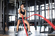 © ty - Fit woman using battle ropes during strength training at the gym.