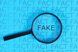 Concept for Fake News with words 'fact' in row and single word  'fake' highlighted by magnifying glass on blue background