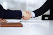 © rogerphoto - Business people shaking hands while sitting at the desk at meeting or negotiation, close-up. Group of unknown businessmen in a modern office. Teamwork, partnership and handshake concept