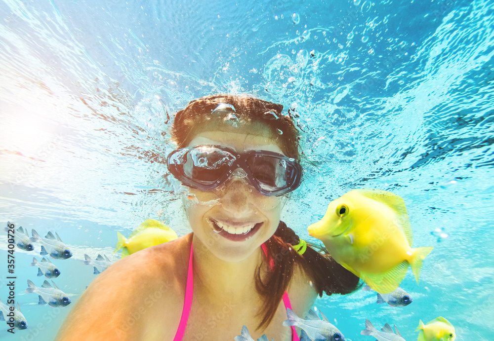 Smiling little girl in swim goggles swimming underwater in pool ...