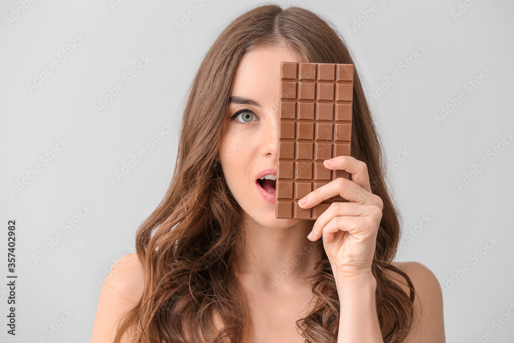 Beautiful young woman with tasty chocolate on light  background