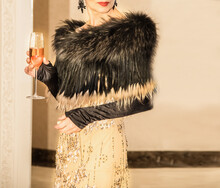 Beautiful Elegant Stylish Woman In A Beautiful Cocktail Dress Of Gold Color, A Fur Cape Of Black With Beige Flowers, In Long Black Gloves, Dainty Earrings Made Of Stones In The Ears